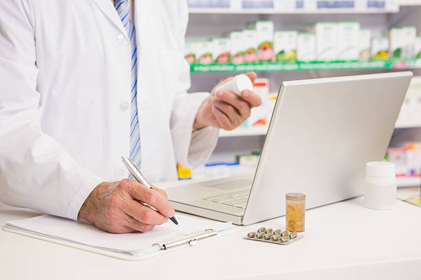 Pharmacist writing on clipboard and holding medication in the pharmacy